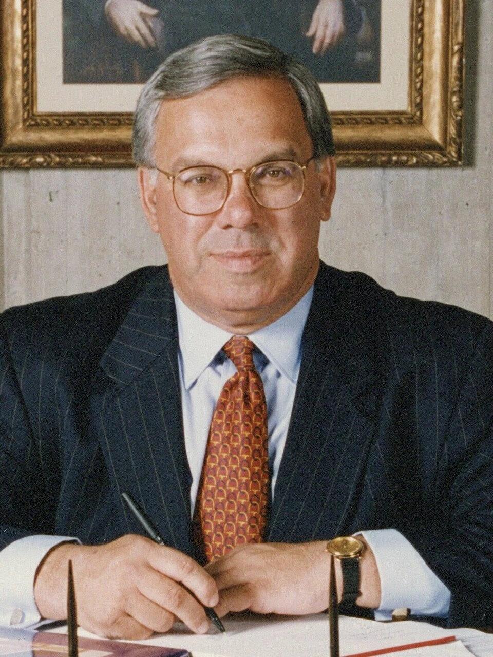Thomas Menino seated at a desk in a formal suit and tie, portrait photo.